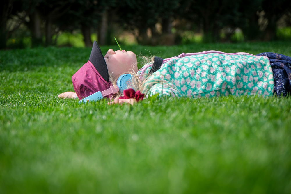 Kind liegt im Gras, Kopfhörer auf und lässt die Sonne auf sich scheinen